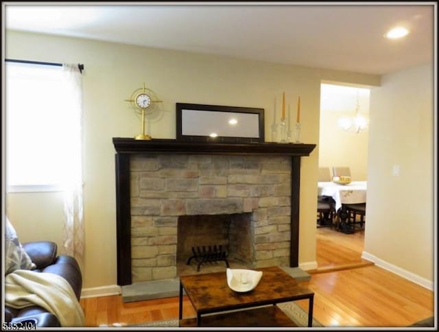 living area featuring a fireplace with raised hearth, baseboards, recessed lighting, and wood finished floors