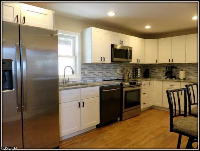 kitchen with appliances with stainless steel finishes, tasteful backsplash, a sink, light stone counters, and white cabinetry