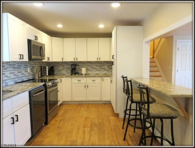 kitchen featuring range with electric stovetop, backsplash, stainless steel microwave, black dishwasher, and light wood-style flooring