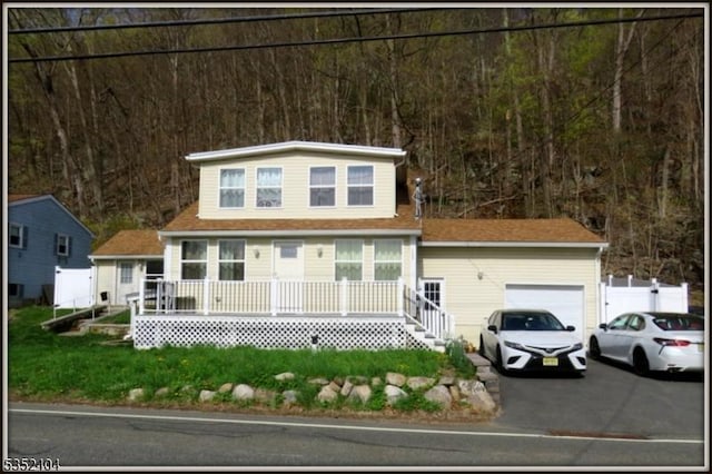 view of front of house featuring covered porch, an attached garage, a wooded view, and aphalt driveway