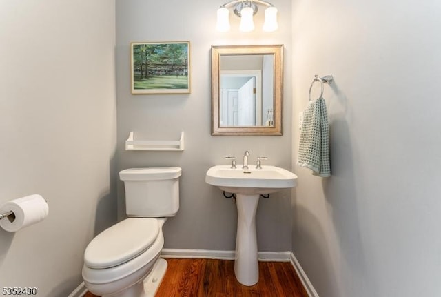half bath with baseboards, wood finished floors, and toilet