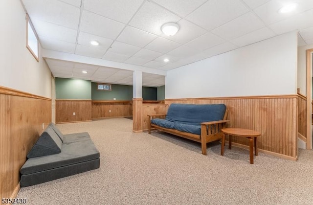 living area with wooden walls, a paneled ceiling, carpet flooring, and wainscoting