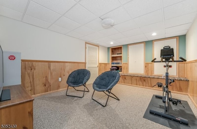 exercise room featuring carpet, a wainscoted wall, and a drop ceiling