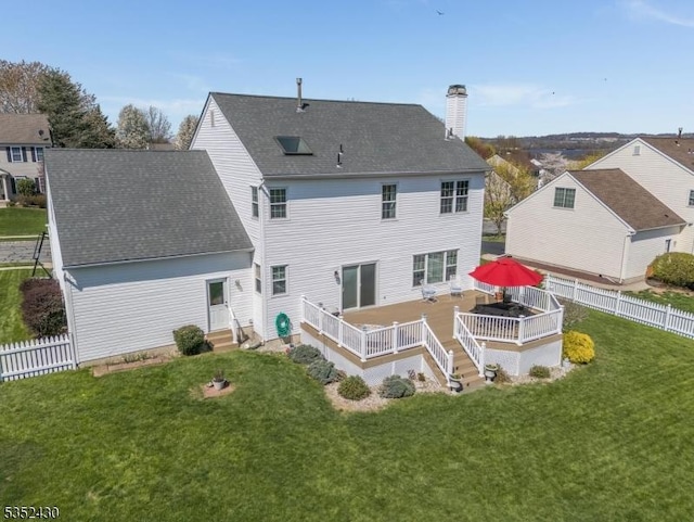 rear view of property featuring a fenced backyard, a chimney, a wooden deck, entry steps, and a lawn