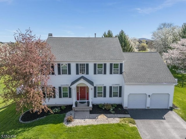 colonial house with an attached garage, a front lawn, aphalt driveway, and roof with shingles