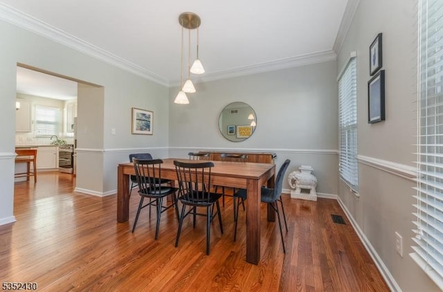 dining room with visible vents, baseboards, wood finished floors, and ornamental molding