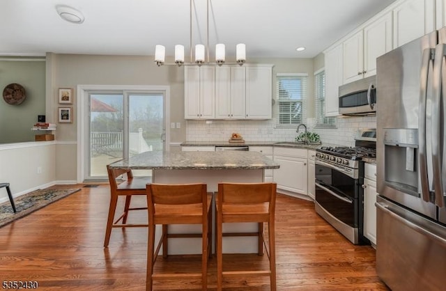 kitchen featuring white cabinets, stainless steel appliances, a sink, a center island, and a kitchen bar