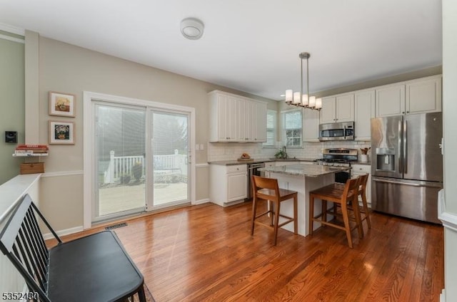 kitchen with white cabinets, stainless steel appliances, dark wood finished floors, decorative backsplash, and a breakfast bar area