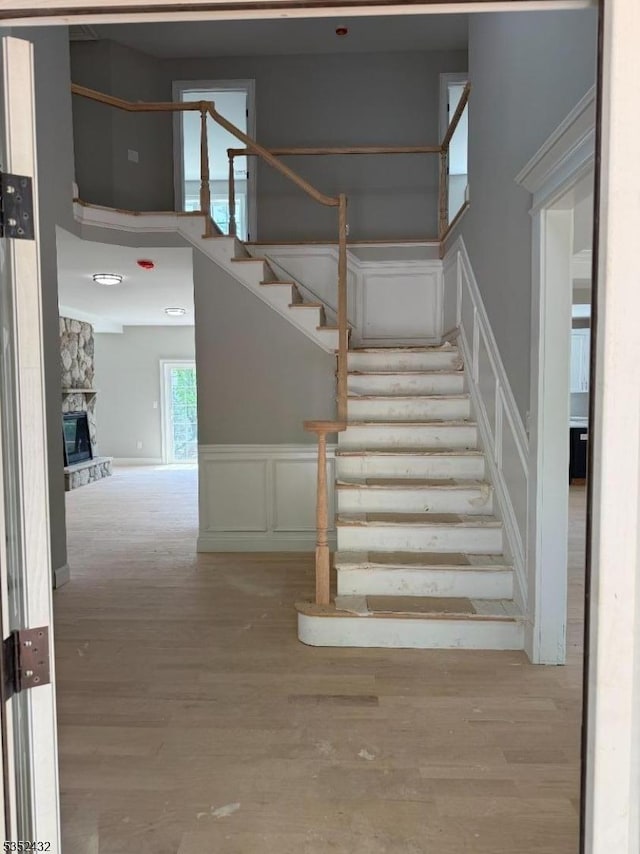 stairs featuring wainscoting, a stone fireplace, a decorative wall, and wood finished floors