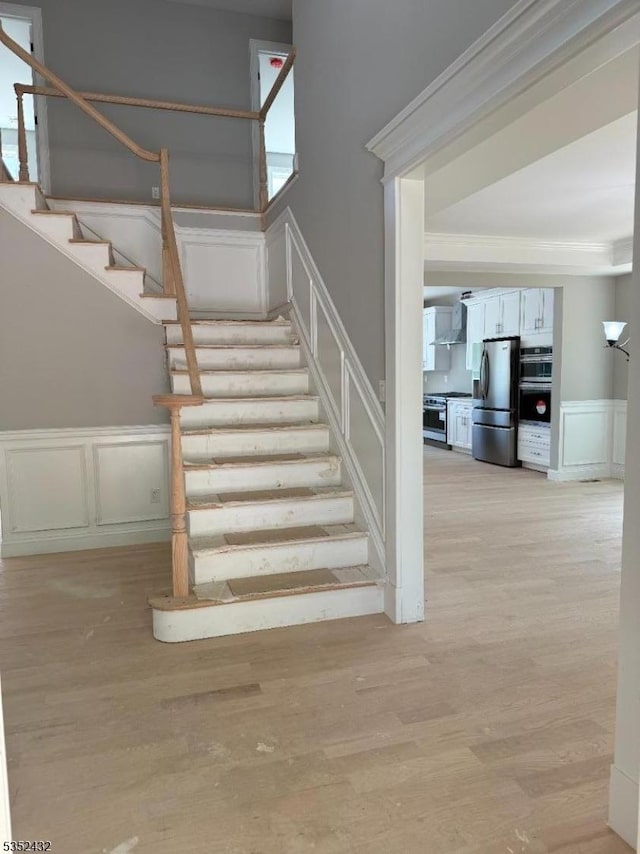 staircase featuring crown molding, a wainscoted wall, wood finished floors, and a decorative wall