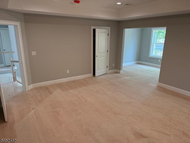 empty room with crown molding, baseboards, light wood-type flooring, recessed lighting, and a raised ceiling