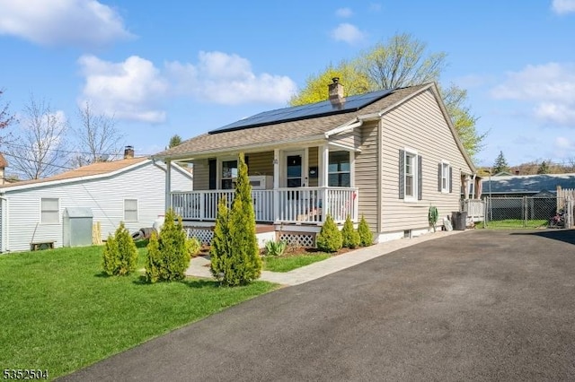 bungalow-style home with aphalt driveway, a chimney, covered porch, solar panels, and a front lawn