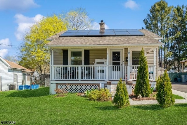 view of front of house featuring a front yard, central air condition unit, covered porch, a chimney, and solar panels