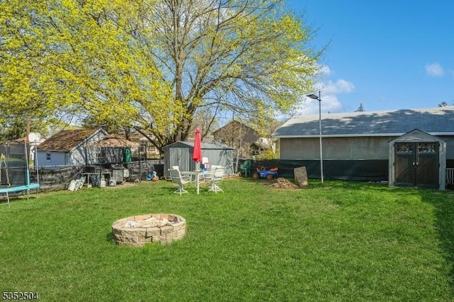 view of yard with a trampoline, an outdoor fire pit, an outdoor structure, a storage unit, and fence