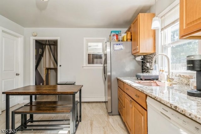 kitchen with light stone countertops, a sink, white dishwasher, decorative light fixtures, and freestanding refrigerator