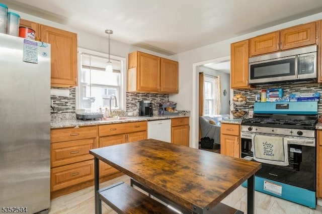 kitchen with a sink, stainless steel appliances, pendant lighting, and backsplash