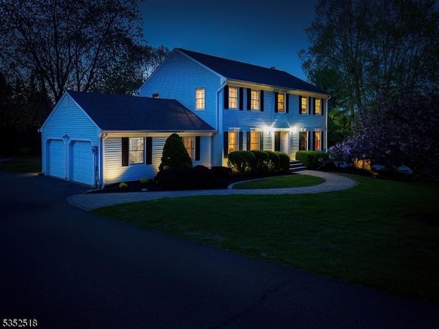 colonial home with an attached garage, a front lawn, and driveway