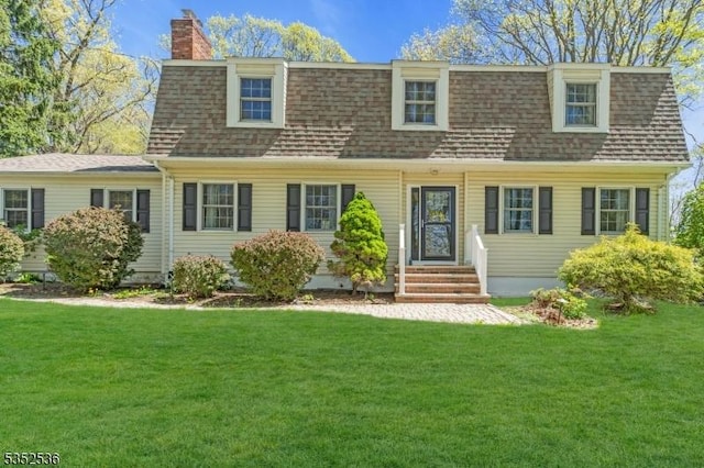 view of front of home with entry steps, a front yard, a chimney, and roof with shingles