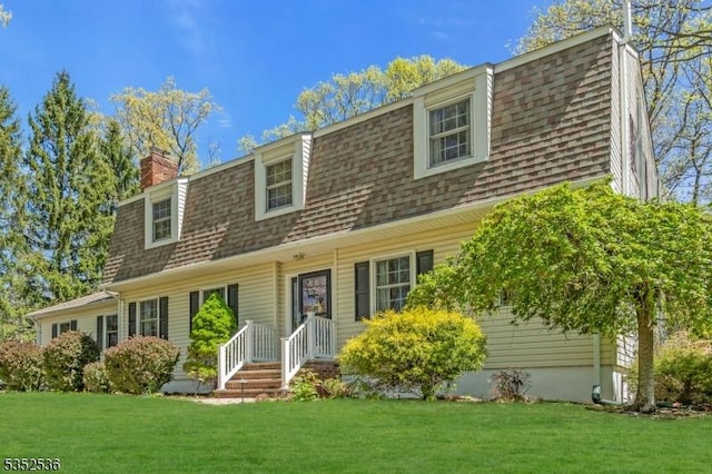 view of front of home featuring a chimney, a shingled roof, and a front yard