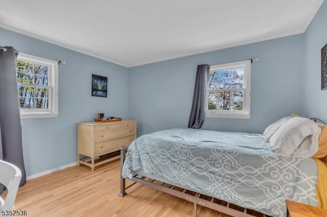 bedroom with baseboards, multiple windows, ornamental molding, and light wood-type flooring