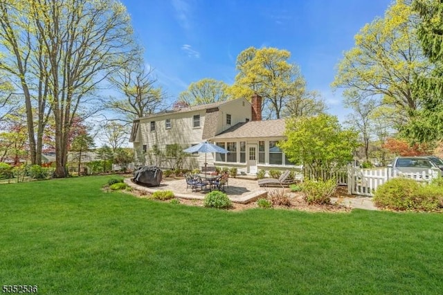 rear view of house featuring a lawn, fence, a chimney, and a patio area