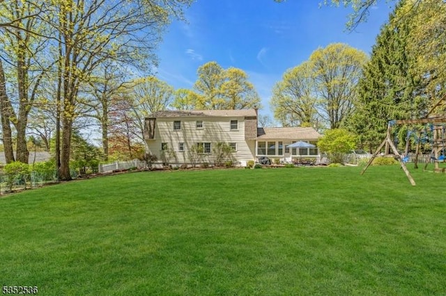 rear view of property with a lawn, fence, and a playground