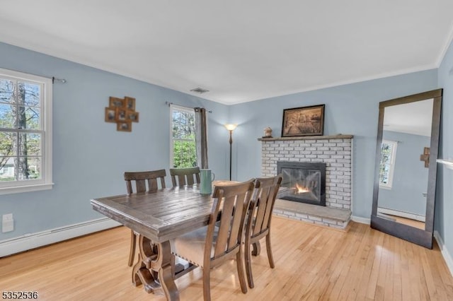 dining area featuring visible vents, a brick fireplace, a baseboard radiator, a baseboard heating unit, and light wood-style floors
