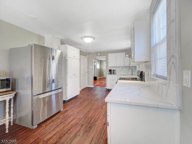 kitchen featuring white cabinetry, decorative backsplash, appliances with stainless steel finishes, light stone countertops, and wood finished floors
