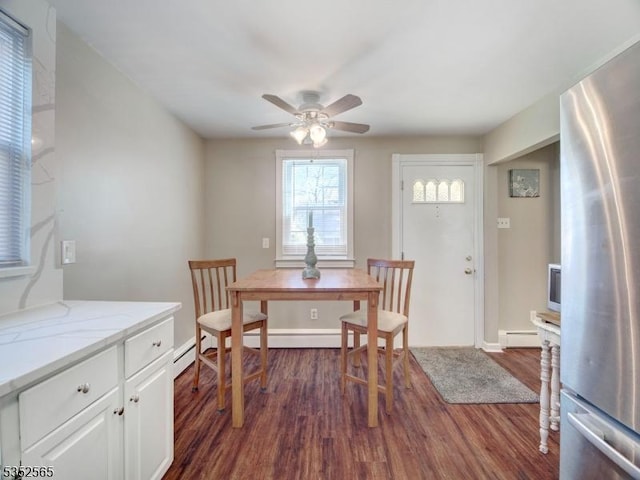 dining area featuring dark wood-style floors, baseboard heating, a ceiling fan, and baseboards