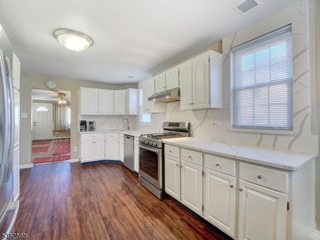 kitchen with white cabinets, a sink, stainless steel appliances, under cabinet range hood, and dark wood finished floors