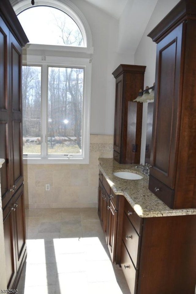bathroom with tile walls, tile patterned flooring, wainscoting, vanity, and lofted ceiling