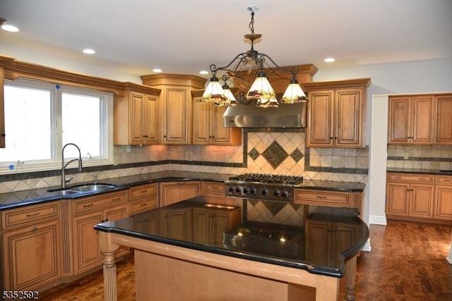 kitchen with dark countertops, a notable chandelier, ventilation hood, a sink, and stainless steel gas stovetop