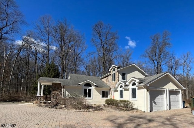 view of front facade featuring a garage, driveway, stone siding, and stucco siding
