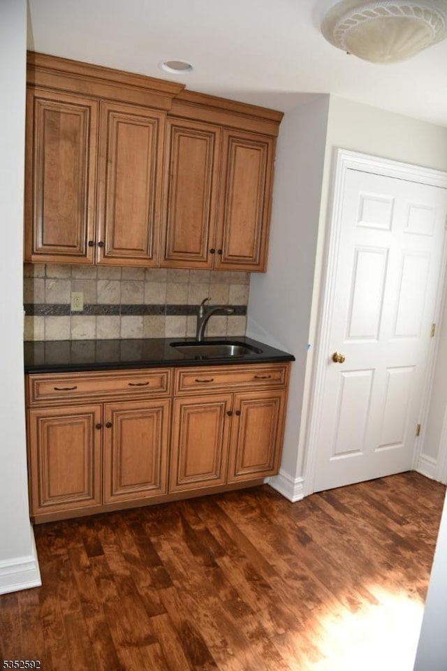 kitchen with dark wood-style flooring, dark countertops, tasteful backsplash, brown cabinets, and a sink