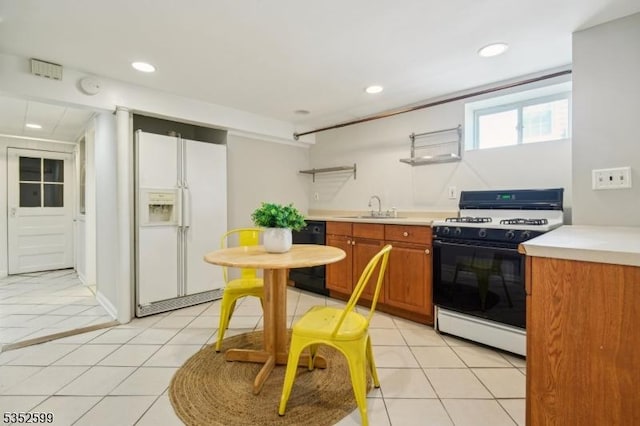 kitchen with a sink, light countertops, white fridge with ice dispenser, black dishwasher, and range with gas cooktop