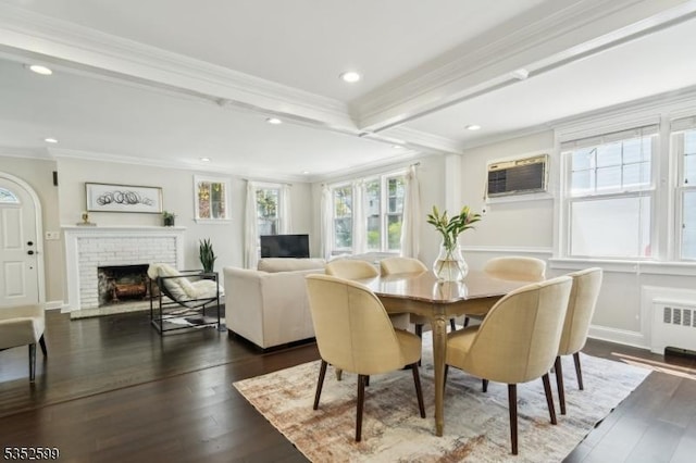 dining space with dark wood-type flooring, ornamental molding, radiator heating unit, and a fireplace