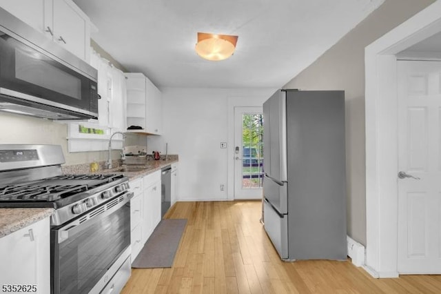 kitchen featuring appliances with stainless steel finishes, a sink, light wood-style floors, and white cabinetry