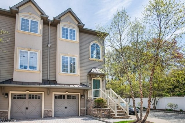 multi unit property with fence, stone siding, a garage, a standing seam roof, and driveway