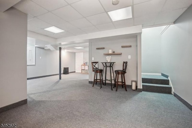 finished below grade area featuring carpet floors, a paneled ceiling, baseboards, and a community bar