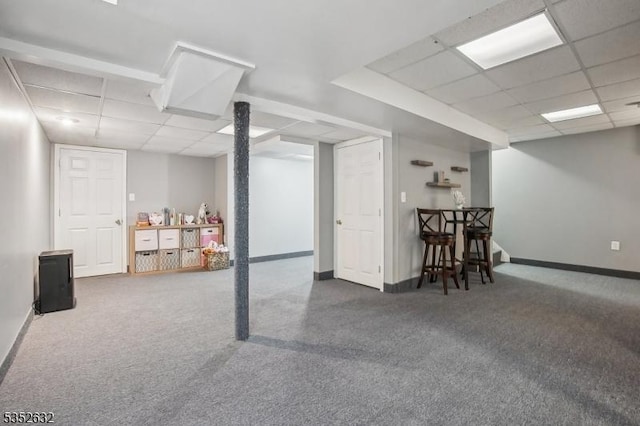 finished below grade area featuring a paneled ceiling, carpet, and baseboards