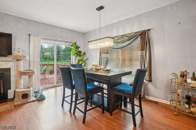 dining room featuring wood finished floors, a chandelier, baseboards, and a fireplace with raised hearth