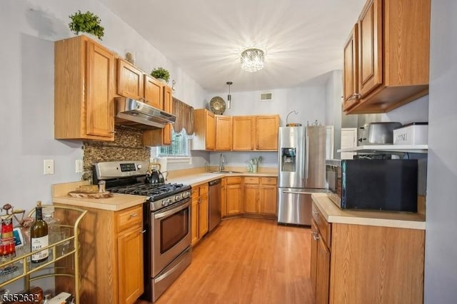 kitchen with stainless steel appliances, a sink, under cabinet range hood, light countertops, and light wood-style floors