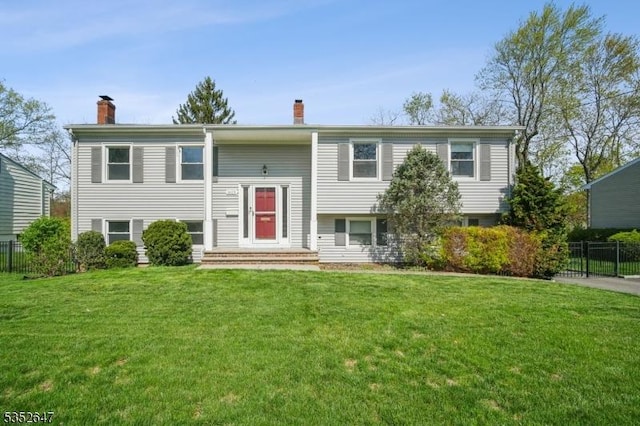 bi-level home with a front lawn, fence, and a chimney