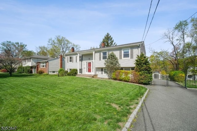 bi-level home with a front lawn, fence, a chimney, a gate, and driveway