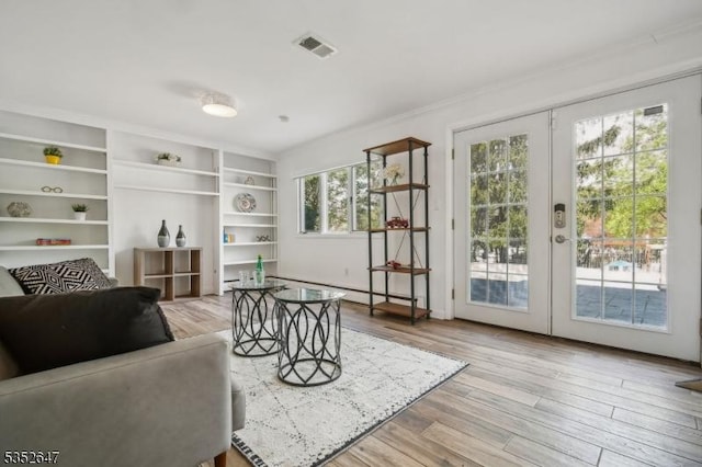 living room featuring light wood-style floors, ornamental molding, french doors, and visible vents
