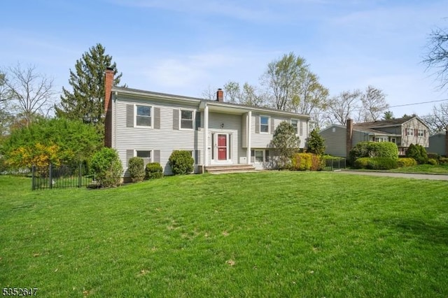 raised ranch with fence, a chimney, and a front lawn