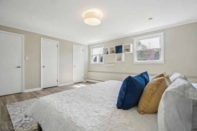bedroom featuring ornamental molding, wood finished floors, two closets, baseboards, and a baseboard heating unit