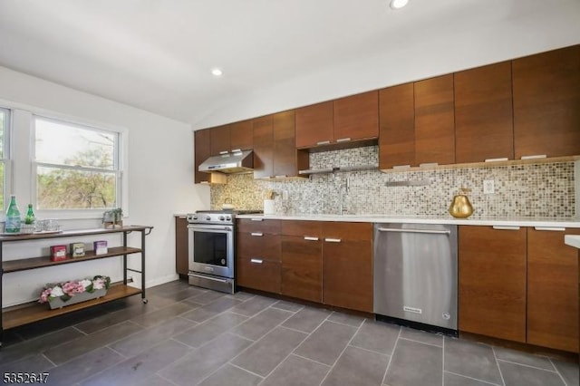 kitchen with decorative backsplash, vaulted ceiling, light countertops, under cabinet range hood, and stainless steel appliances