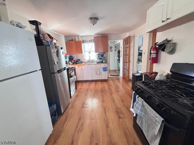 kitchen featuring black gas range oven, light countertops, light wood finished floors, and freestanding refrigerator