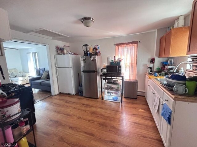 kitchen with a baseboard heating unit, black microwave, light wood finished floors, and freestanding refrigerator